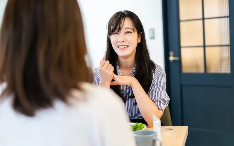 飲食店のテーブルで食事をしながら話す2人